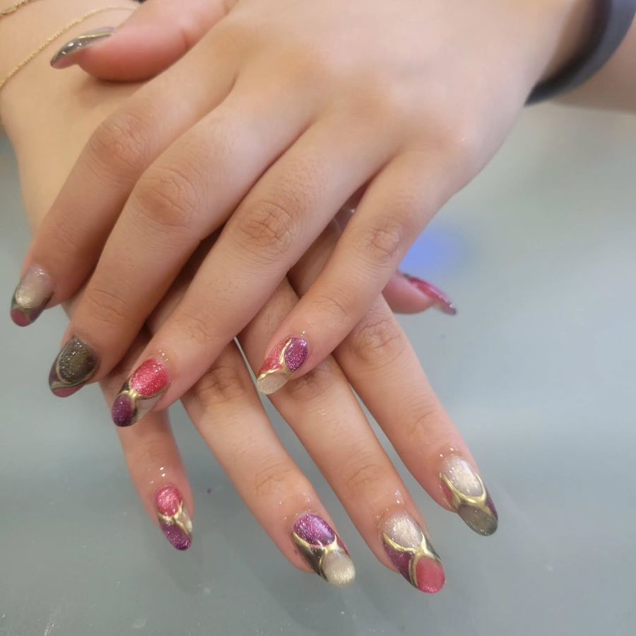 Close-up of almond-shaped nails with pink, purple and gold glitter nail art by Jess Nailz and Spa