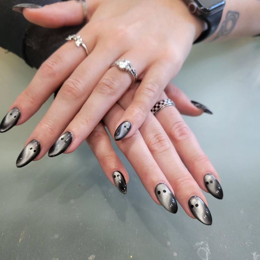 Almond-shaped nails with dark metallic cat-eye polish and small ghost designs